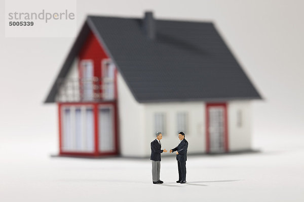 Zwei Miniaturunternehmerfiguren  die vor einem Haus die Hand schütteln