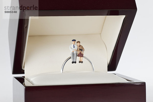 Miniaturfiguren einer älteren Frau und eines älteren Mannes auf einem Ehering sitzend