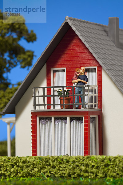 Eine Miniatur-Vaterfigur hält seine Tochter auf dem Balkon eines Puppenhauses.