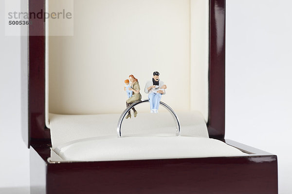 Miniaturfiguren einer jungen Familie auf einem Ehering in einem Schmuckkästchen sitzend