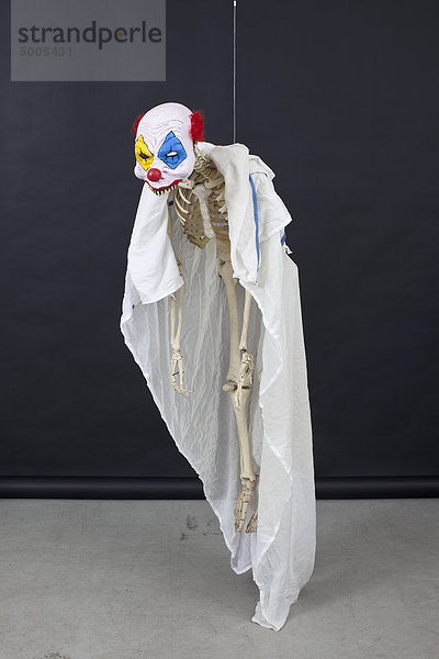Hängendes Skelett mit Clownmaske.