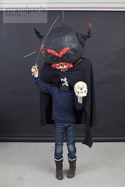 Kind mit Halloween-Outfit  einem Totenkopf in der Hand und einem Spielzeugschwert.