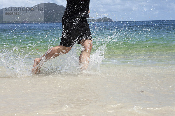 Niedriger Abschnitt eines Mannes  der am Strand durchs Wasser läuft.
