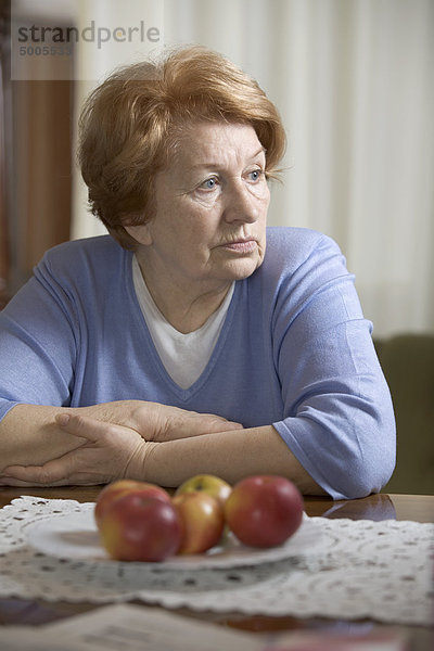 Eine ältere Frau  die an einem Tisch sitzt und traurig aussieht.