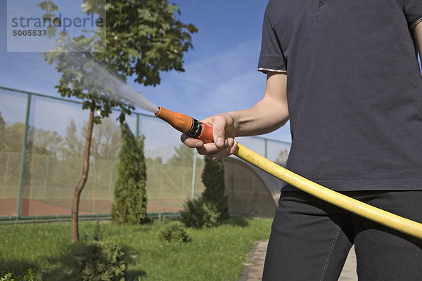 Ein Teenager spritzt einen Gartenschlauch in einem Hinterhof.