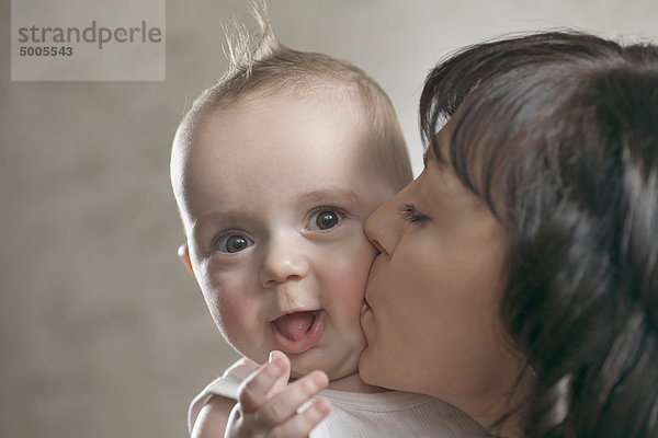 Ein überraschtes Baby  das von seiner Mutter geküsst wird.