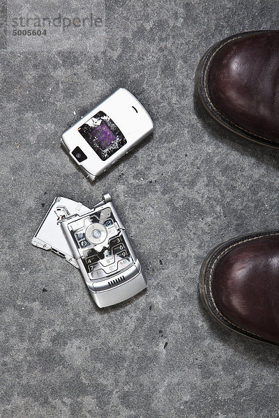Zwei gestiefelte Füße neben einem zerschmetterten Handy
