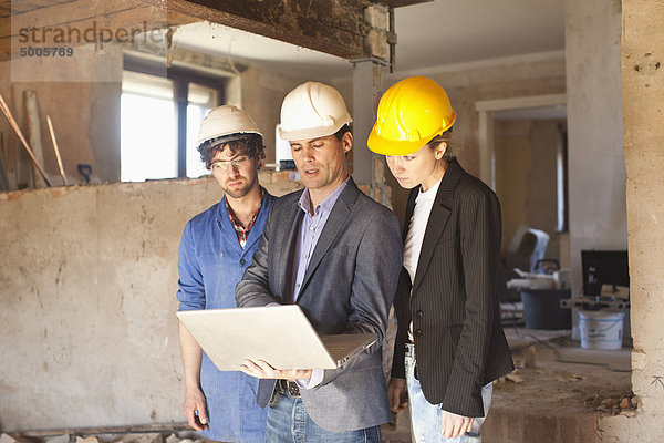 Ein Bauunternehmer und Architekten beim Betrachten eines Laptops auf einer Baustelle