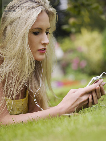 Eine Frau  die im Gras liegt und einen MP3-Player hört.