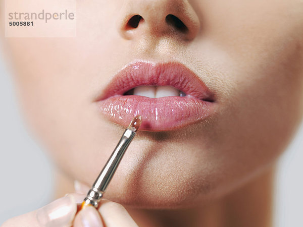 Eine Frau  die Lipgloss mit einem Make-up-Pinsel aufträgt  Nahaufnahme der Lippen und des Mundes.