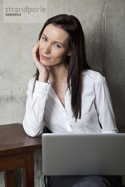 Eine Geschäftsfrau mit einem Laptop  der die Kamera anlächelt.