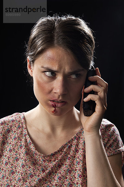 Eine geschlagene Frau  die ein schnurloses Telefon benutzt.