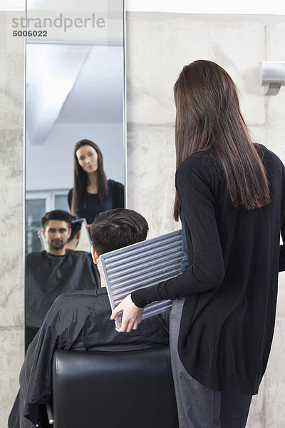 Ein Friseur hält einen Spiegel für einen Kunden  Rückansicht