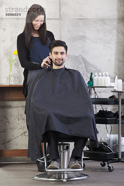 Ein Friseur  der bei einem männlichen Kunden eine Haarschneidemaschine benutzt.