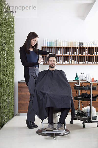Ein Friseur  der das Haar eines Kunden besprüht.