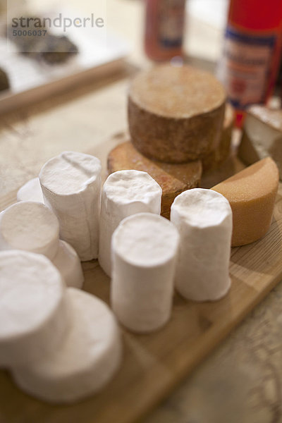 Verschiedene verpackte Käsesorten auf Holzschneidebrett auf Tisch