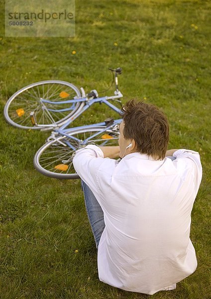 Mann sitzt im Gras und hört Musik