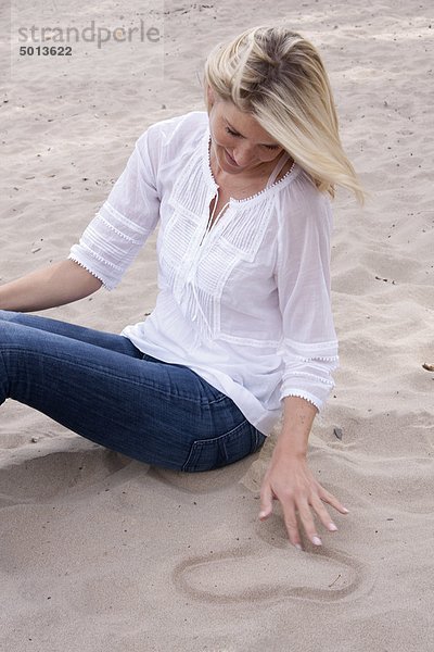 Blonde Frau zeichnet ein Herz in den Sand