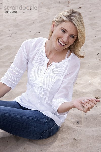 Blonde Frau sitzt im Sand