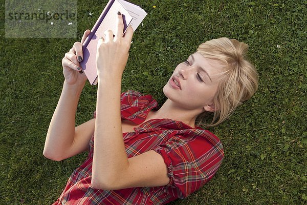 Junge blonde Frau liest ein Buch im Gras