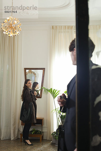 Paar  das sich darauf vorbereitet  das Haus zu verlassen  Mann  der die Frau über die Schulter schaut  während sie sich im Spiegel sieht.