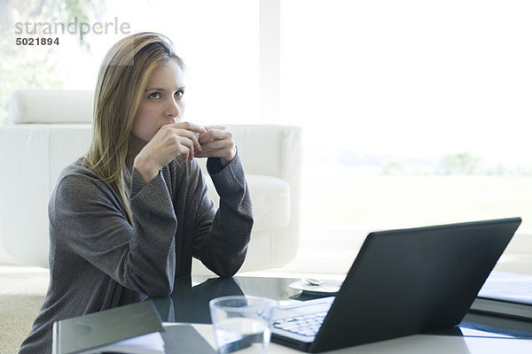 Frau sitzt am Couchtisch mit Laptop und trinkt Kaffee.