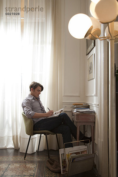 Mann sitzt am Schreibtisch und liest Magazin