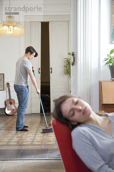 Mann schwingt den Boden zu Hause  Frau schläft im Vordergrund