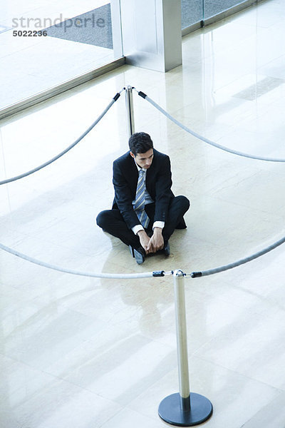 Geschäftsmann sitzend auf dem Boden im abgetrennten Bereich in der Lobby