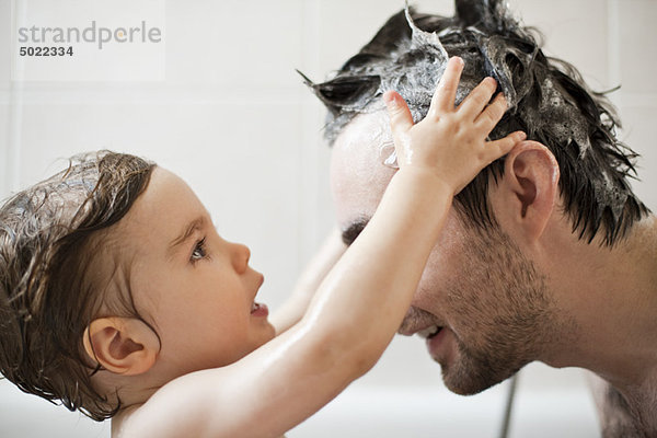 Kleinkind Junge wäscht Vaters Haare im Bad