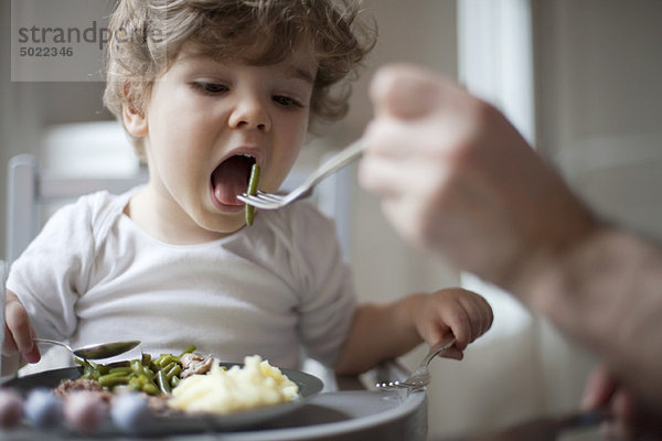 Kleinkind Junge wird mit grünen Bohnen gefüttert.
