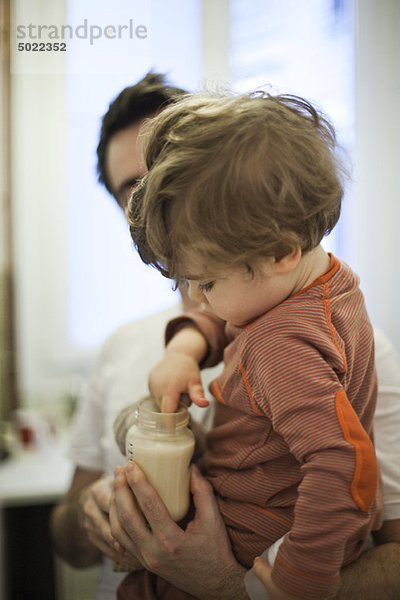 Kleinkind im Arm des Vaters  Test der Milchtemperatur in der Babyflasche