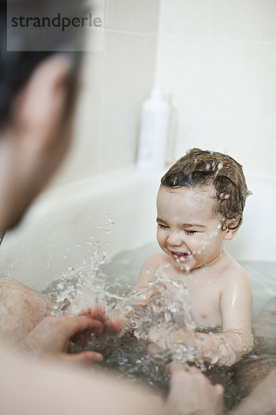 Kleinkind Junge  der mit seinem Vater in der Badewanne spritzt.