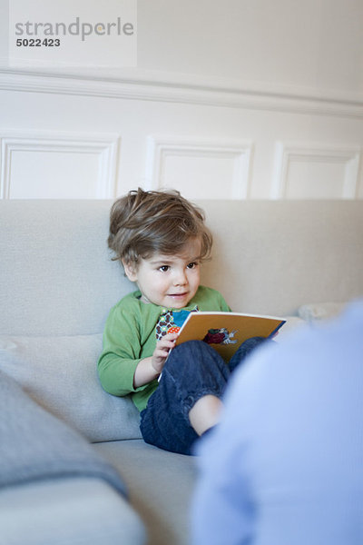Kleinkind Junge sitzend auf der Couch mit Buch in den Händen