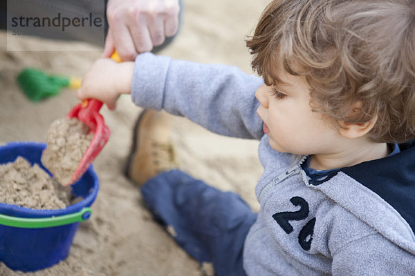 Kleinkind Junge schaufelt Sand in den Eimer
