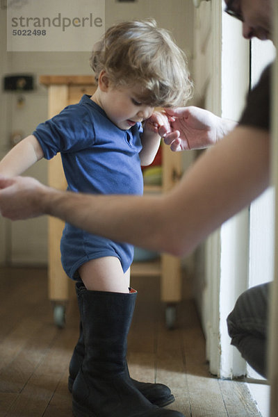 Kleinkind Junge lernt  in Vaters Stiefeln zu laufen.