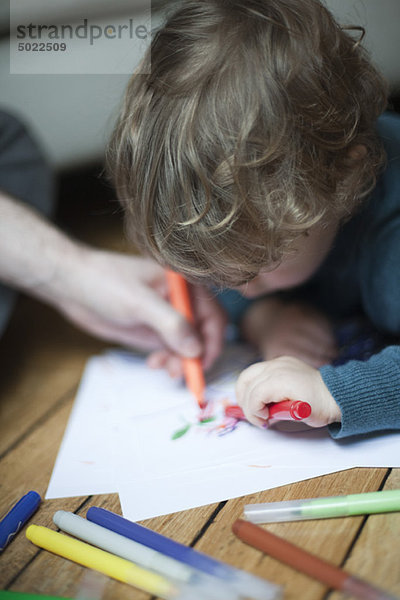 Kleinkind und Elternteil zeichnen zusammen auf Papier