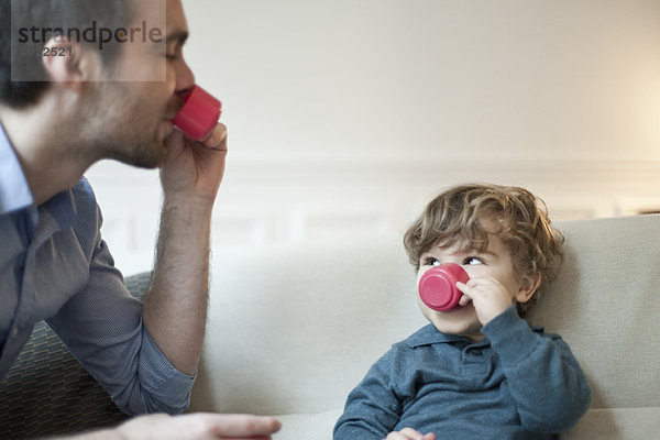 Vater und Kleinkind Sohn tun so  als ob sie Tee mit Spielzeug-Tassen trinken würden.