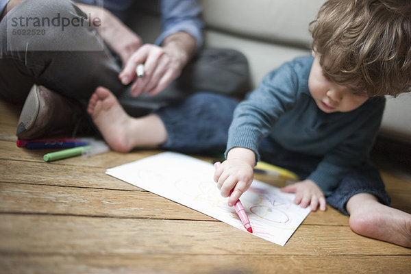 Kleinkind Junge sitzend auf dem Boden mit Elternteil  Zeichnung auf Papier