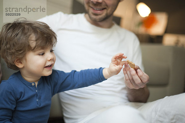 Kleinkind Junge greift nach Keksen in Vaters Hand