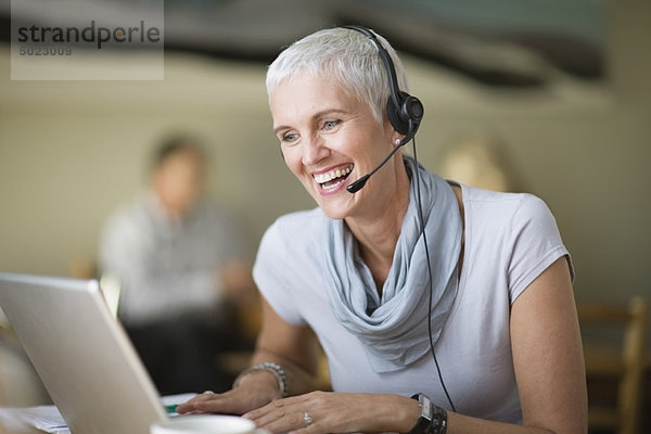 Ältere Frau im Headset mit Laptop