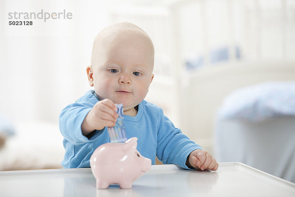 Kleiner Junge  der Geld ins Sparschwein steckt.