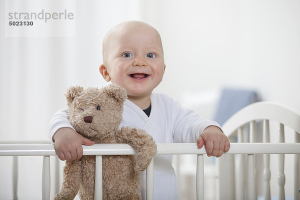 Baby Junge im Kinderbett mit Teddybär