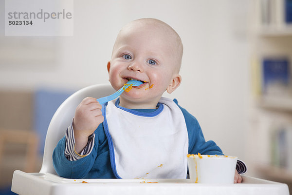 Lächelnder Babyjunge beim Essen im Hochstuhl