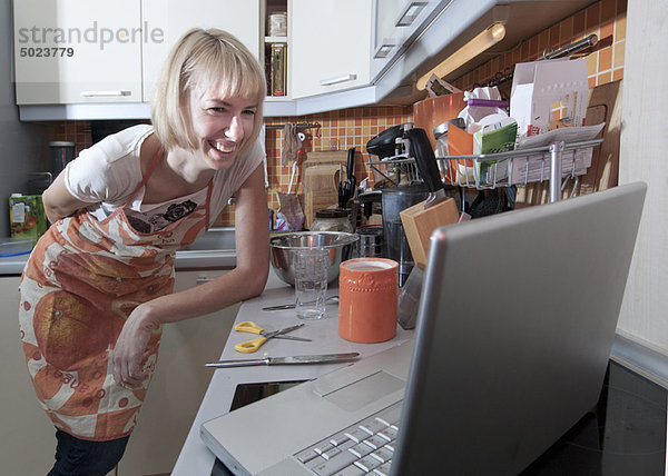 Frau nutzt Laptop zum Kochen in der Küche