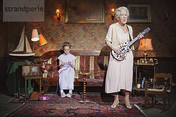 Ältere Frau spielt Gitarre als Mädchen strickt