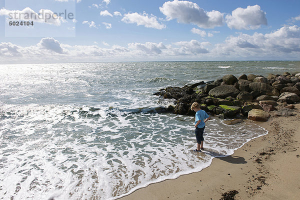 Junge steht in der Brandung am Strand