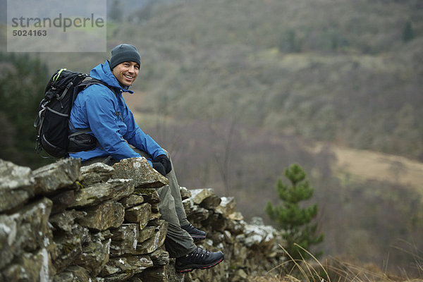 Wanderer auf Steinmauer sitzend