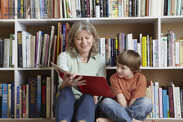Frau liest mit Enkel im Bücherregal