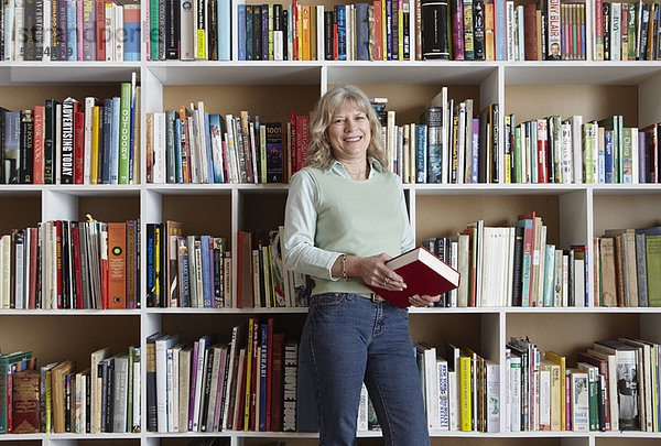 Ältere Frau hält Buch bei den Bücherregalen